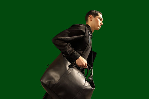 Model carrying a large black bag against a dark green background
